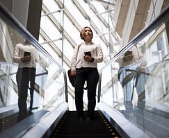 Woman on escalator holding phone, looking up in modern glass building.