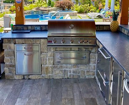 Outdoor kitchen grill under wooden gazebo with "GOOD VIBES" sign, pool.
