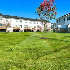 Sprinklers watering lush green lawn behind modern townhouses under clear blue sky. | Down To Earth Landscaping | Jackson New Jersey, USA (732) 833-7702