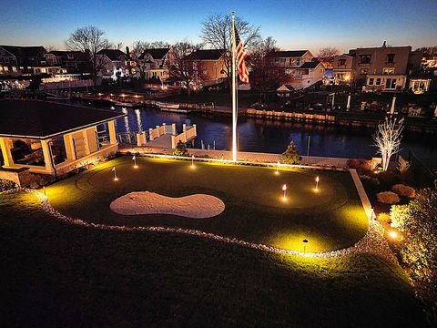Illuminated backyard putting green, sand trap, American flag, canal at night. Residential landscaping near me| Down To Earth Landscaping | Jackson New Jersey, USA (732) 833-7702
