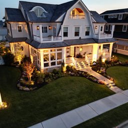 Elegant white house with superbly installed night lighting, American flag, manicured lawn. | Down To Earth Landscaping | Jackson New Jersey, USA (732) 833-7702