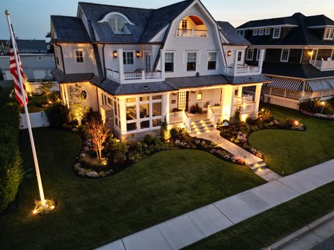 Large luxury house illuminated at dusk with manicured lawn, American flag. Residential landscaping near me| Down To Earth Landscaping | Jackson New Jersey, USA (732) 833-7702