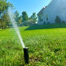 Automatic sprinkler watering a vibrant green lawn next to a house. | Down To Earth Landscaping | Jackson New Jersey, USA (732) 833-7702