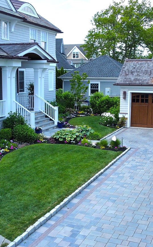 Expansive modern house with porch and professionally installed and maintained lush landscaping, paved driveway, with plants and shrubbery near detached garage. | Down To Earth Landscaping | Jackson New Jersey, USA (732) 833-7702